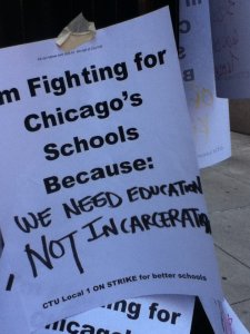 Printed sign reads: "I'm fighting for Chicago's Schools Because," with handwritten text below: "We need education NOT incarceration."