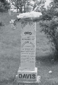 A black and white photo of William Davis's tombstone. It is a white granite pillar reading, “In memory of William Davis, shot in riot at New Waterford power plant, June 11, 1925, Aged 37 years, Asleep in Jesus.”